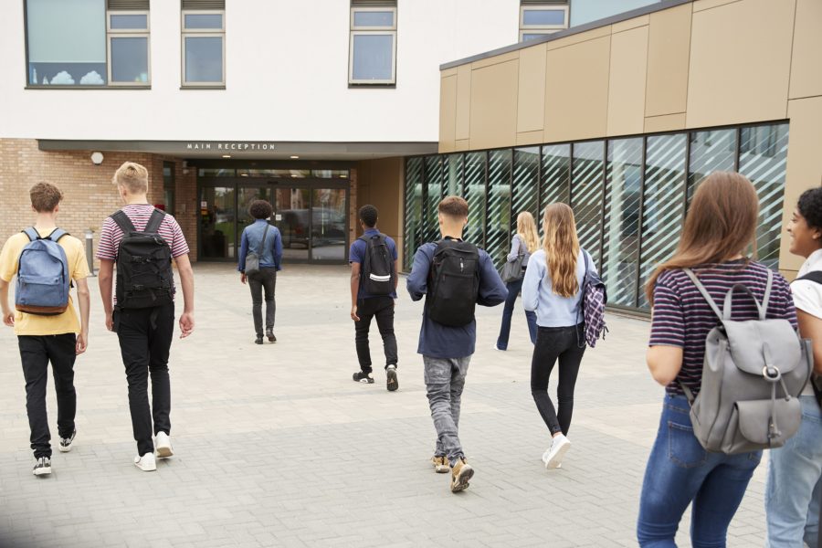 Rear View Of High School Students Walking Into College Building Together